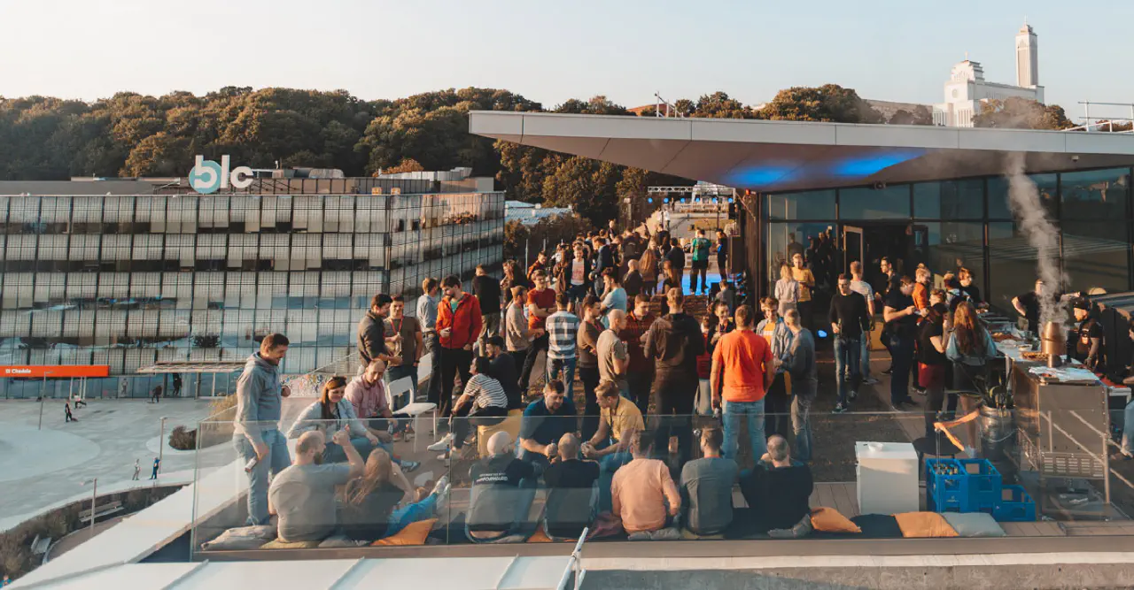 Rooftop event with Adeo Web people socializing near a BBQ, overlooking modern buildings and a tree-covered hill.